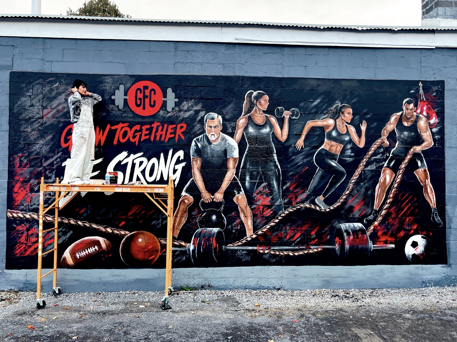 Shima painting the Grow Together mural from a scaffold